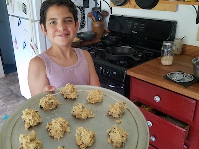 middle schooler holding tray of uncooked cookies in kitchen